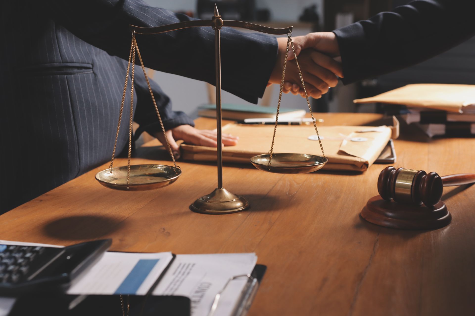 People shaking hands near a balance scale and gavel on a wooden desk.
