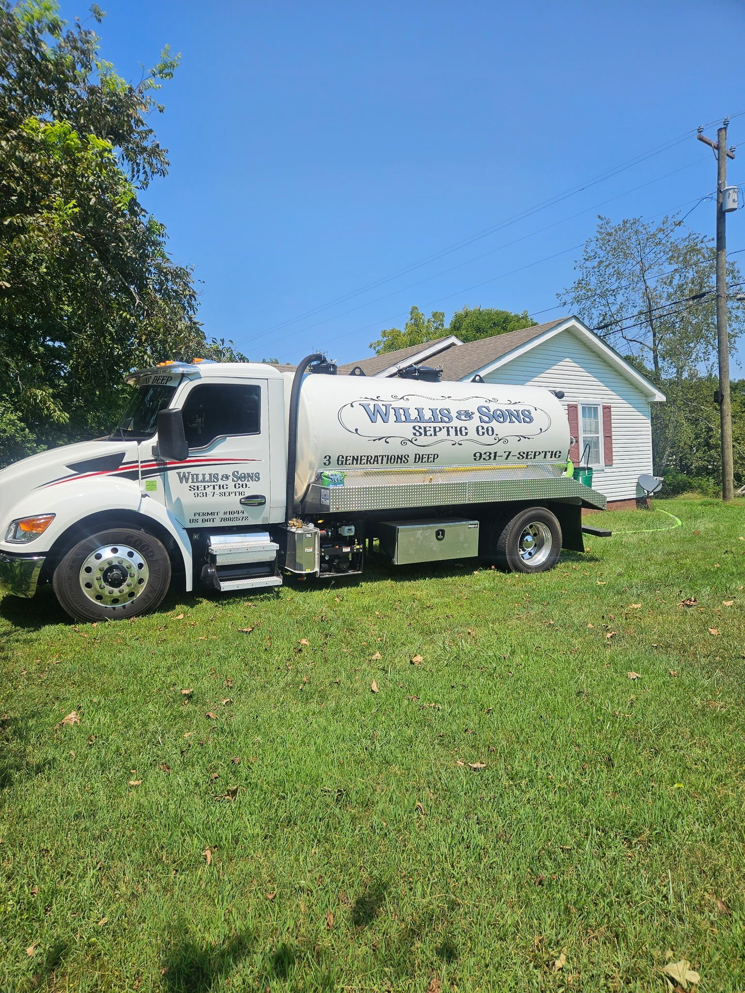 White service truck parked on a grassy lawn beside a house under a clear blue sky.
