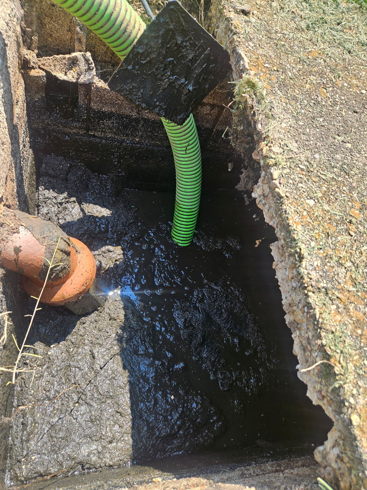Open drain with black water and green corrugated hose in a concrete pit