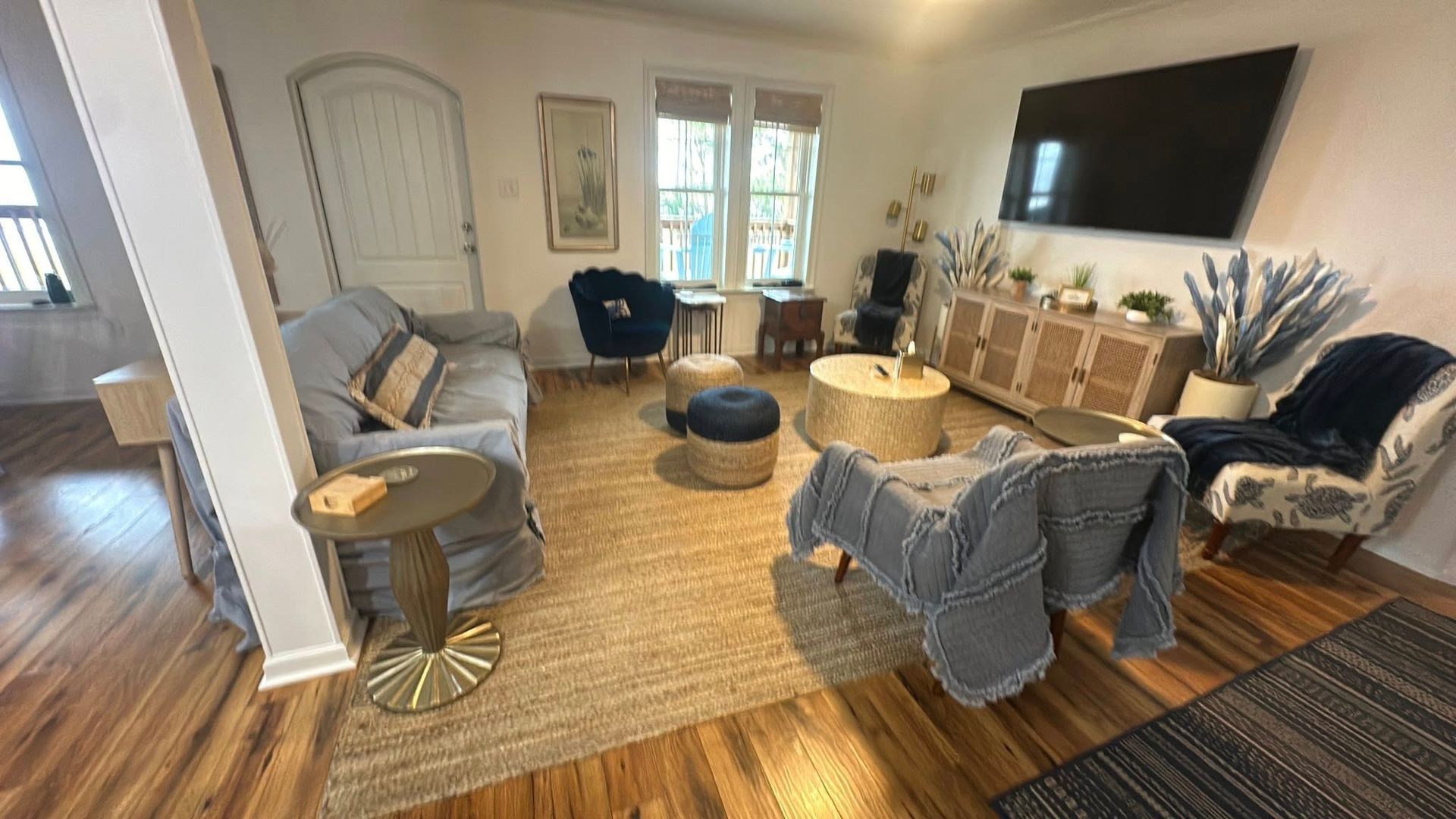 A bright, cozy living room featuring a gray sofa, two accent chairs, a central rug, coffee table, and wall-mounted TV.