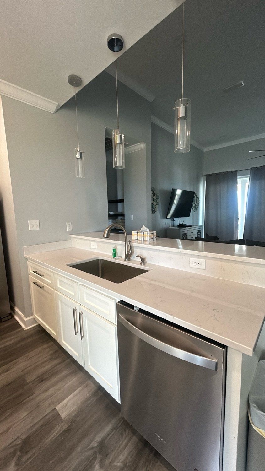 A kitchen island with a stainless steel sink, a dishwasher, white cabinets, and two pendant lights hanging above it.