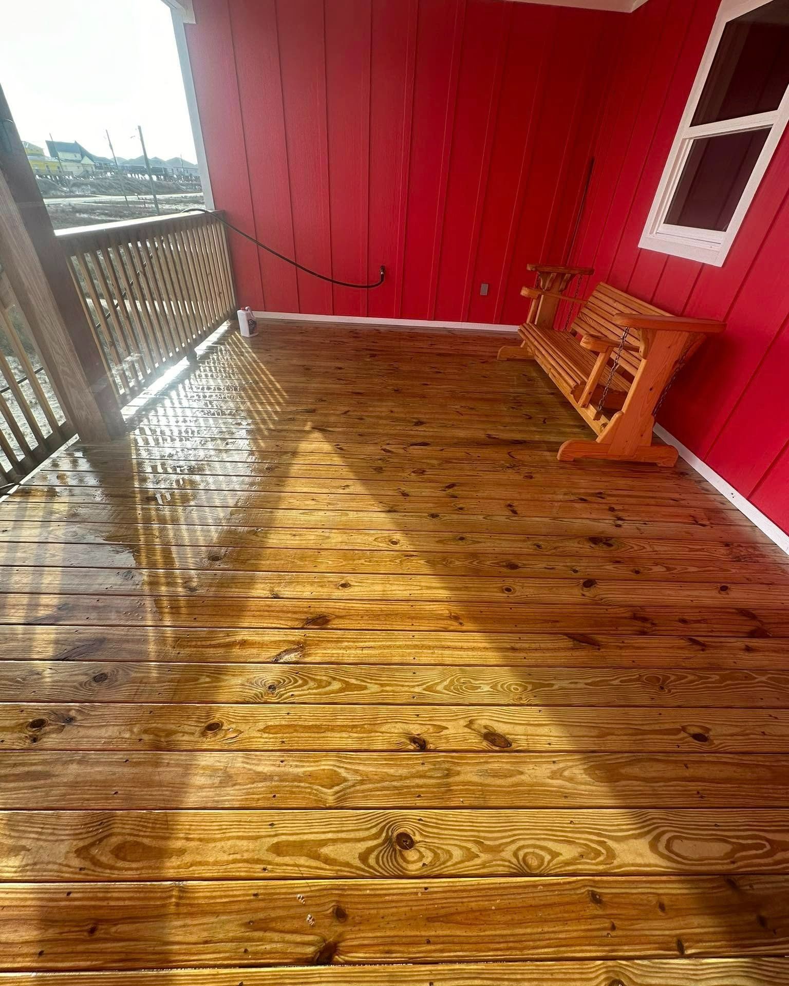 A wooden porch with a red wall and bench, illuminated by a triangular patch of sunlight on the floorboards.