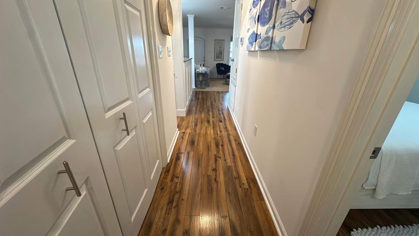 A bright indoor hallway featuring glossy wooden floors, white paneled doors on the left, and abstract wall art.