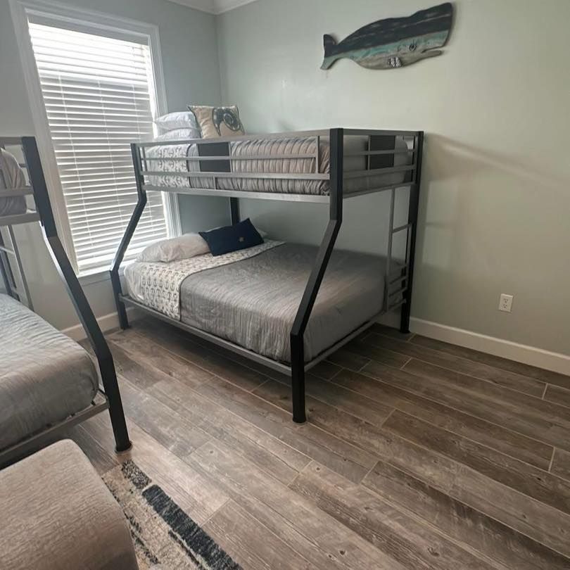 A metal bunk bed with a full-size lower mattress and twin upper bunk in a room with light blue walls and wood-look floors.
