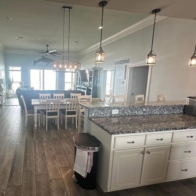 A kitchen with granite counters and white cabinets, opening into a dining area with a long wooden table and chairs.