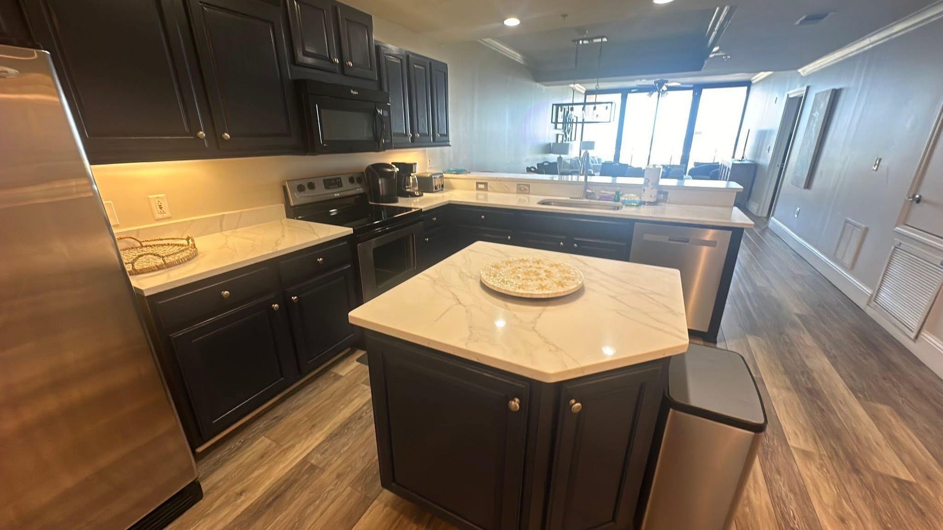A modern kitchen with dark cabinetry, white countertops, a center island, and stainless steel appliances.