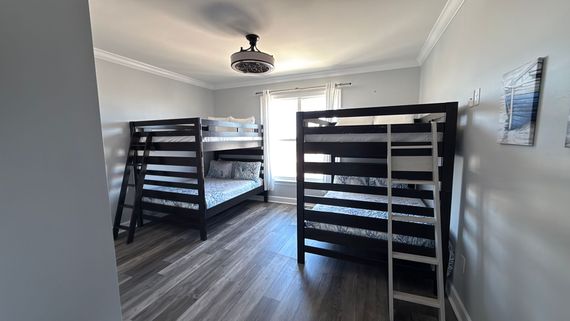 A bedroom featuring two dark wood bunk beds, light gray walls, wood-look flooring, and a ceiling fan.