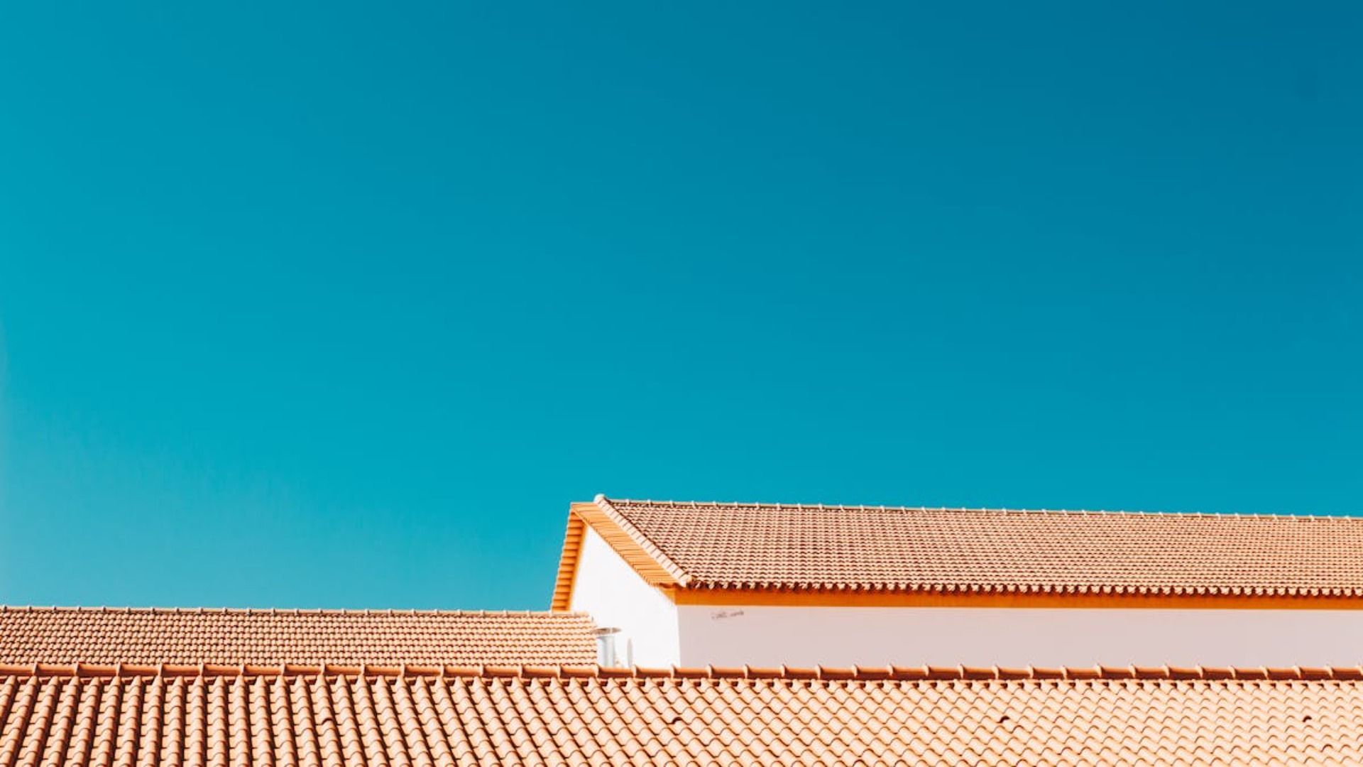 Un edificio blanco con techo de tejas y un cielo azul al fondo.