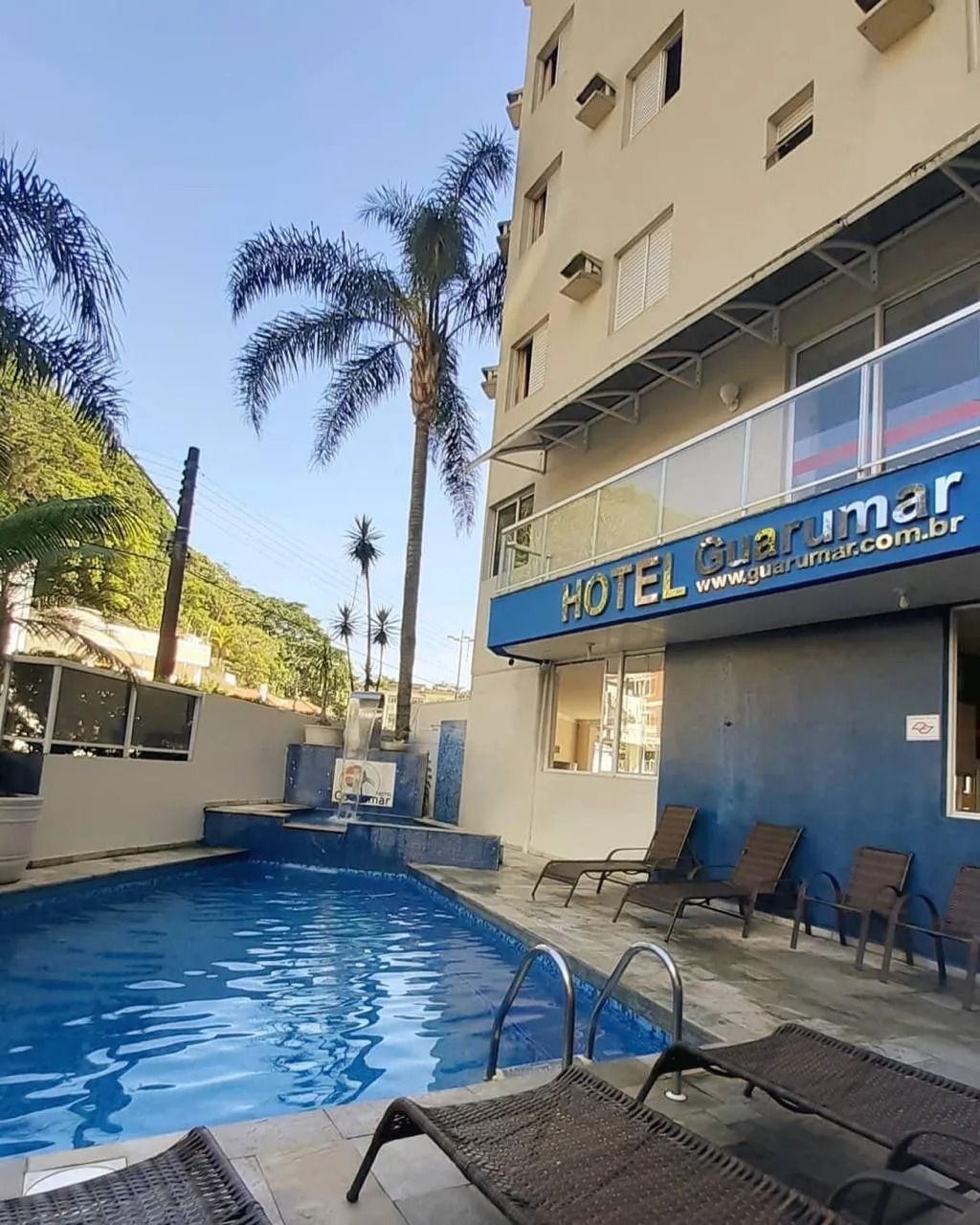 Hotel com piscina: Piscina azul em frente a um prédio de cor clara com placa 