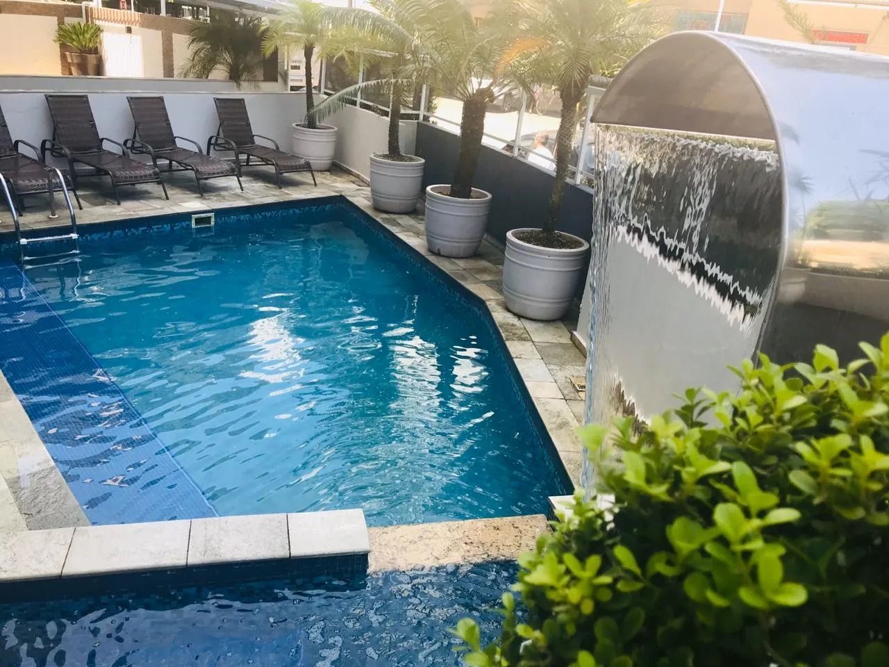 Piscina com cascata, espreguiçadeiras e vasos de plantas.