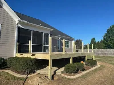 A screened in porch with a wooden deck in front of a house.
