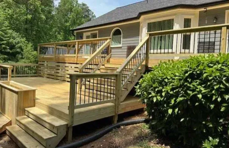 A large wooden deck with stairs is in front of a house.