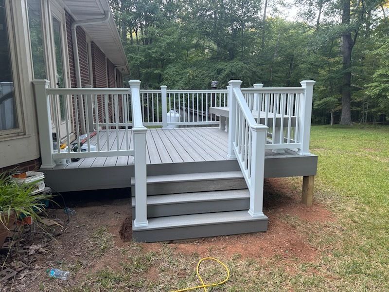 Gray deck with white railing and stairs, beside a house and yard with trees.