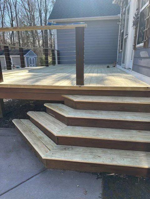 Wooden deck with steps leading to a yard, featuring a railing with cable and brown steps.