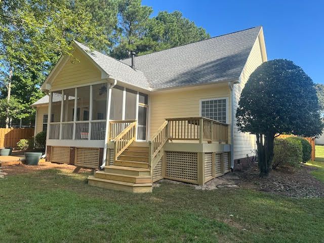 A yellow house with a screened in porch and a wooden deck.