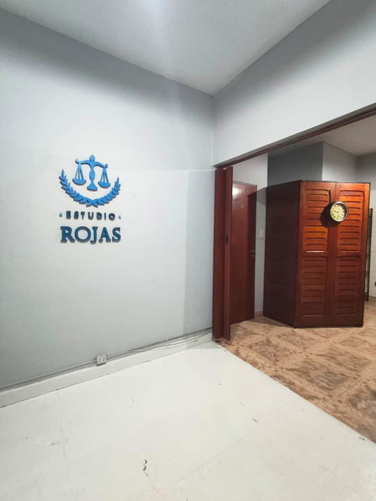 Rincón del vestíbulo con el logotipo de “Estudio Rojas” en la pared, paredes grises, suelo blanco y puerta abierta.