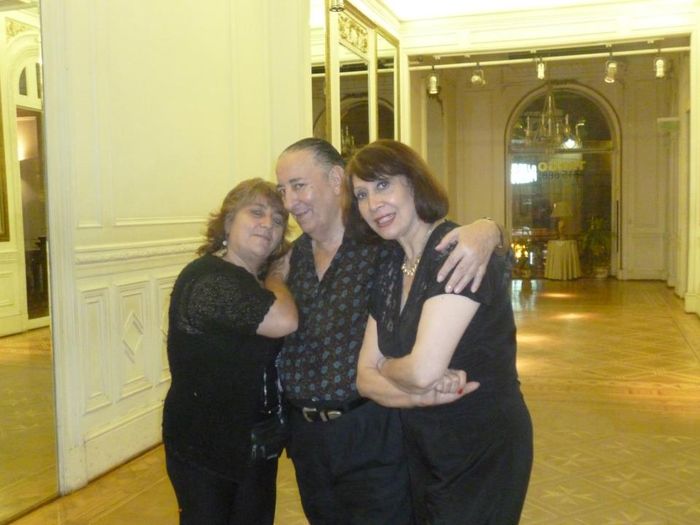 Tres personas, abrazadas, posan en una habitación grande y elegante.