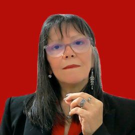 Mujer con gafas y cabello oscuro, vestida con un blazer negro, top rojo y pendientes, sobre un fondo rojo.