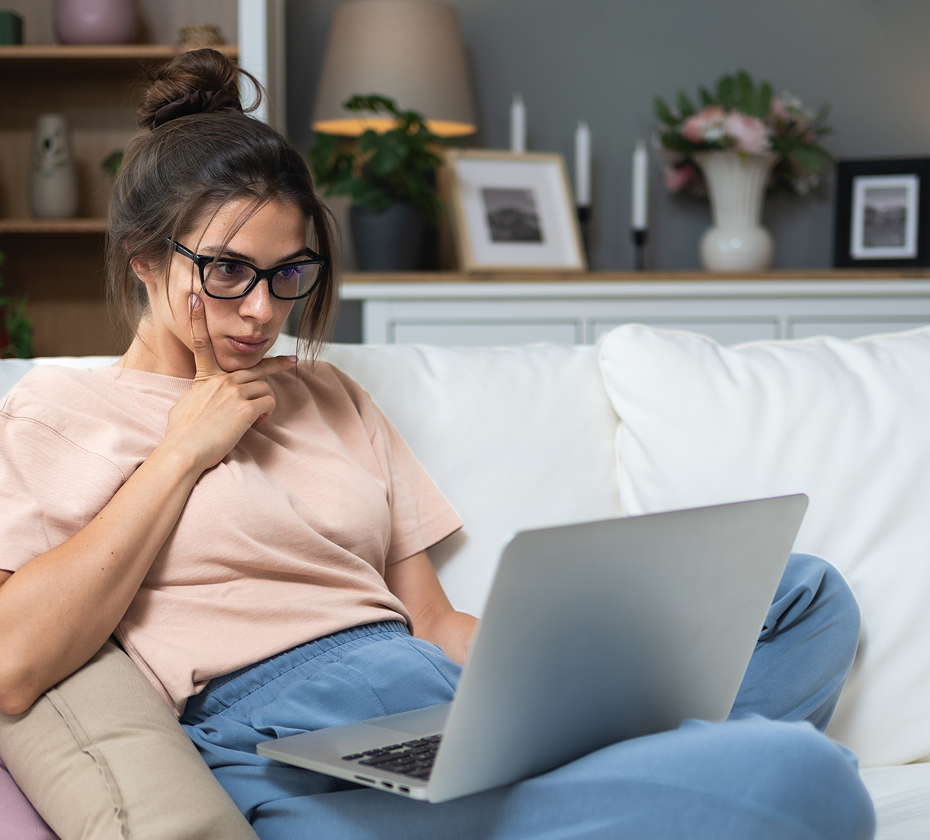 Woman with glasses using a laptop on a couch in a cozy living room