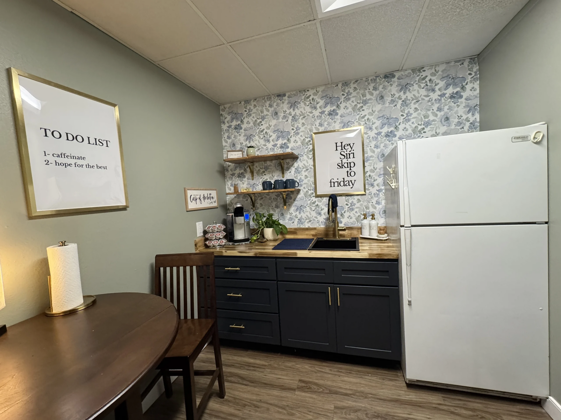 Small kitchen nook with white fridge, dark cabinets, patterned backsplash, and round table by the wall