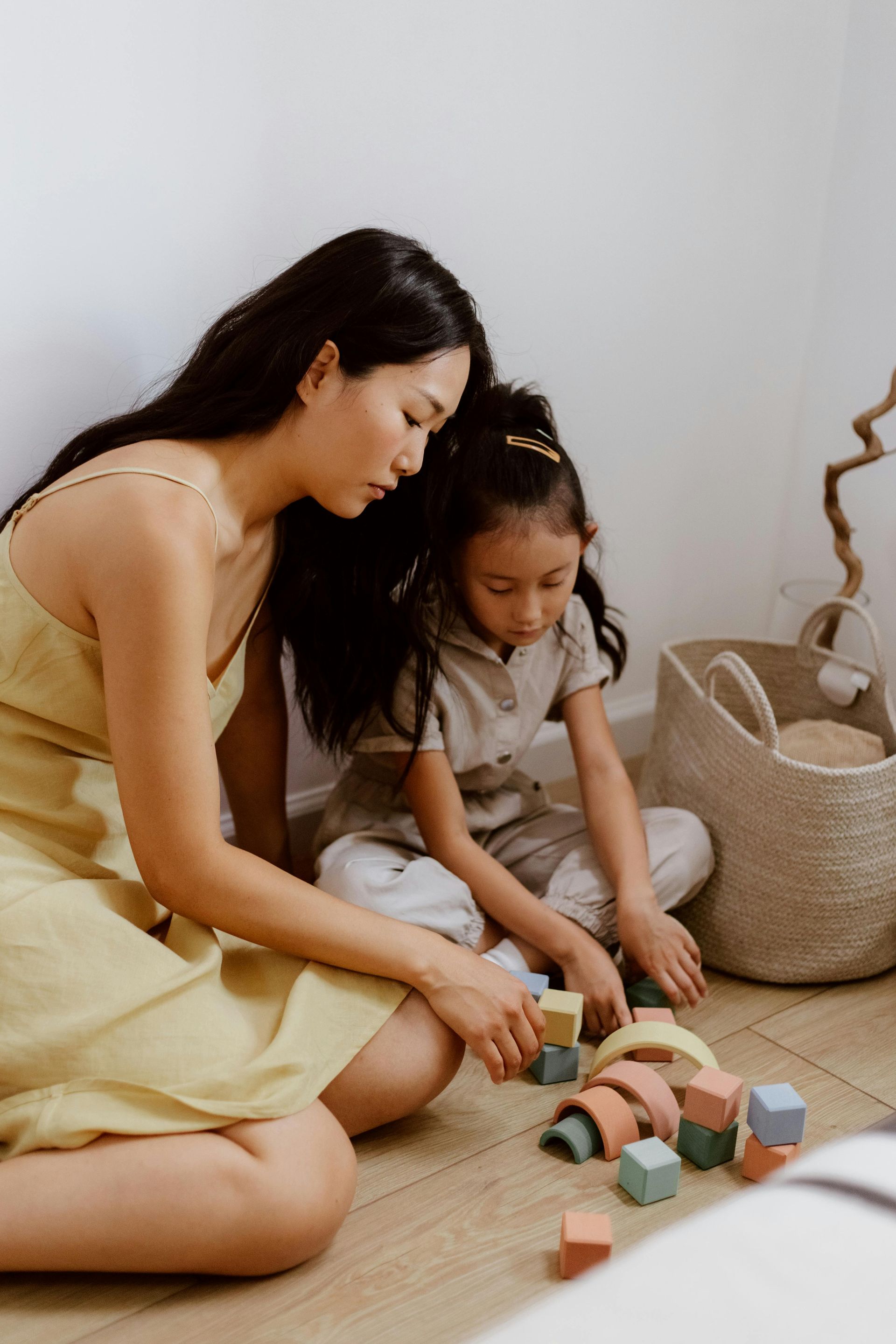 Two people sitting on the floor, stacking colorful wooden blocks in a bright room