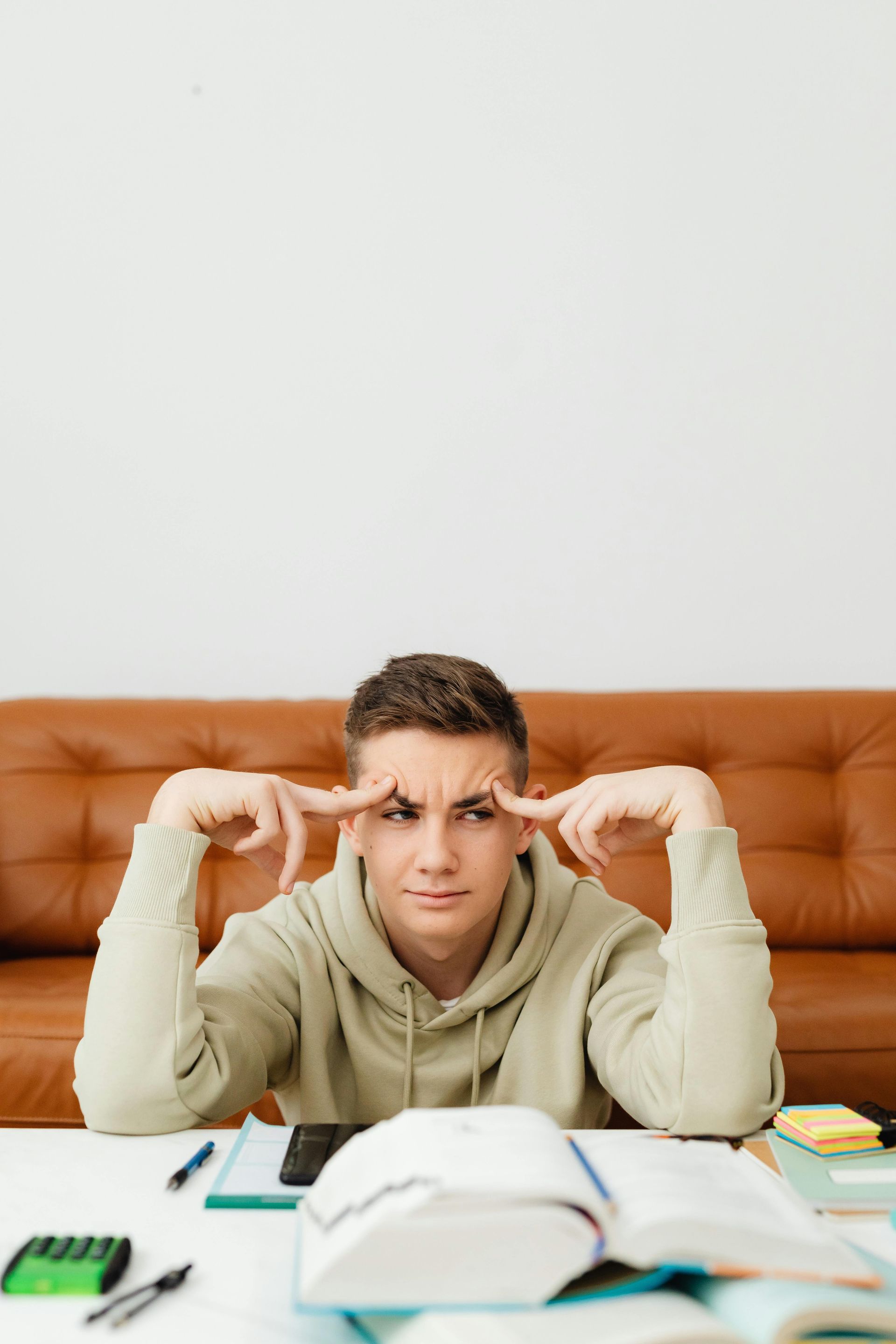Frustrated person at a desk, pointing to their temples with books and notes spread out.