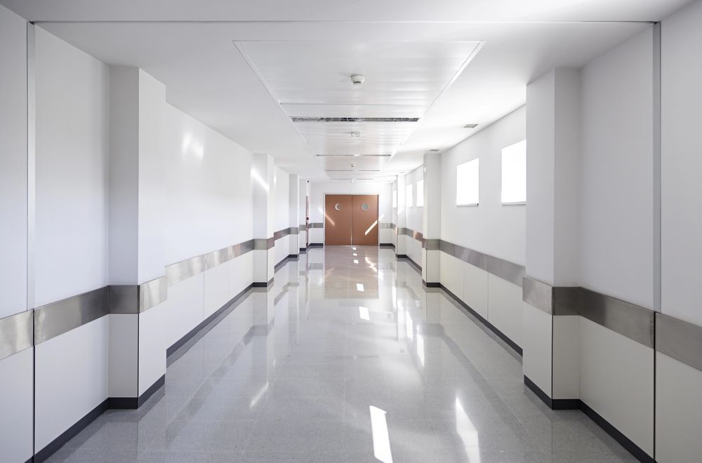 Long, bright hospital corridor, white walls, shiny floor, door at the end.