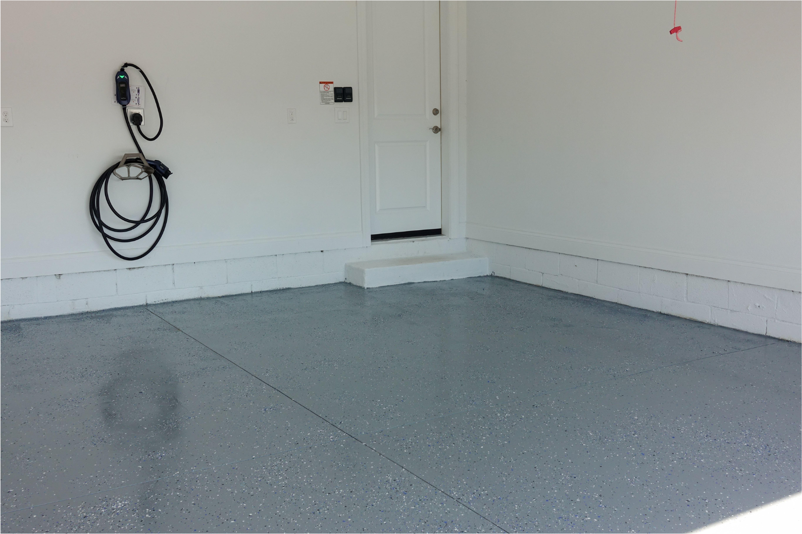Gray epoxy garage floor with white walls and a door. An EV charger is mounted on the wall.