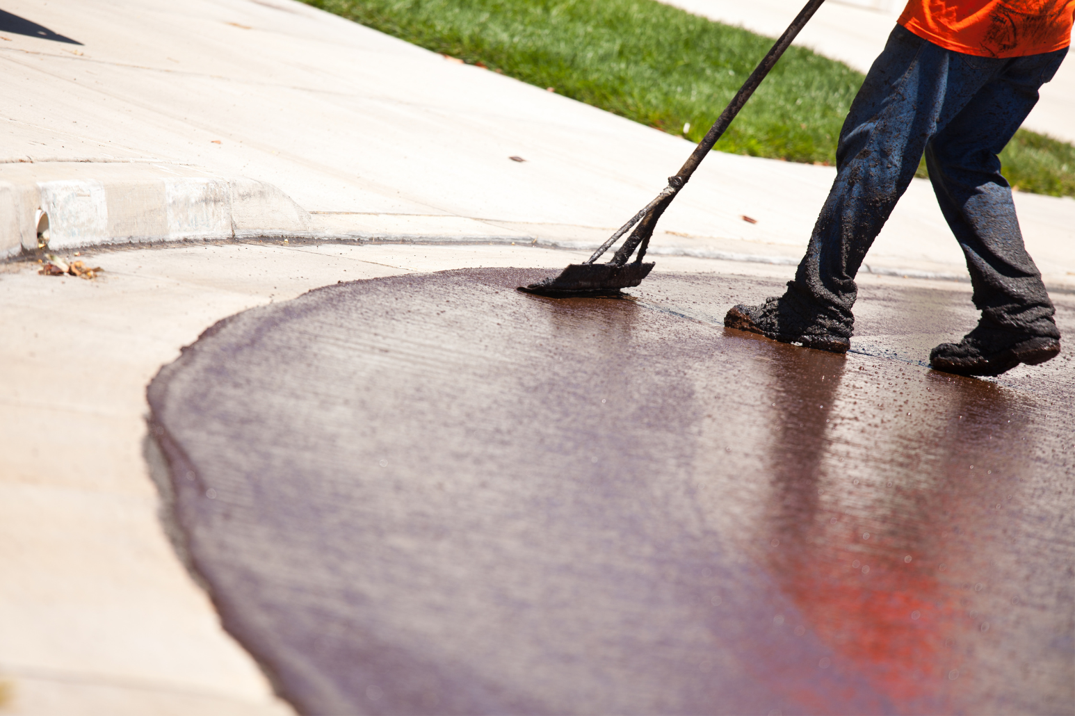 Person spreads dark asphalt on a curved concrete surface with a long-handled tool.
