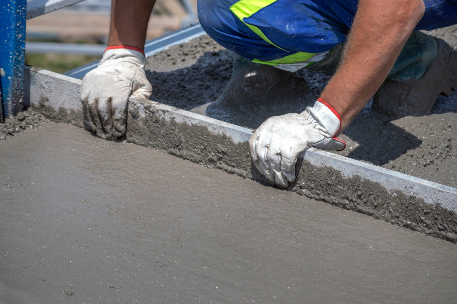 Construction worker smoothing wet concrete with a tool, outdoors.