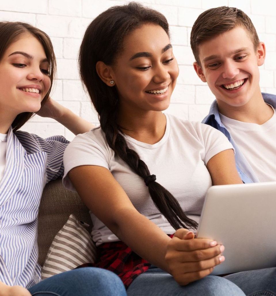Three people are sitting on a couch looking at a tablet