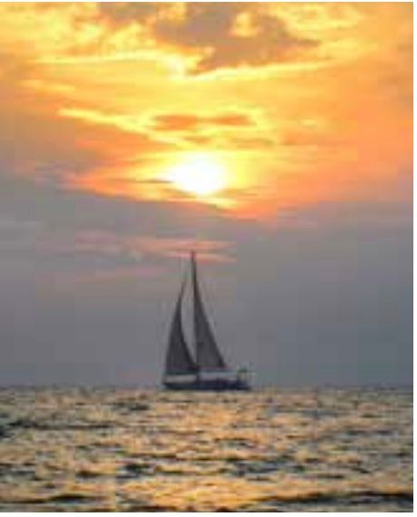 A sailboat is floating on top of a large body of water at sunset.