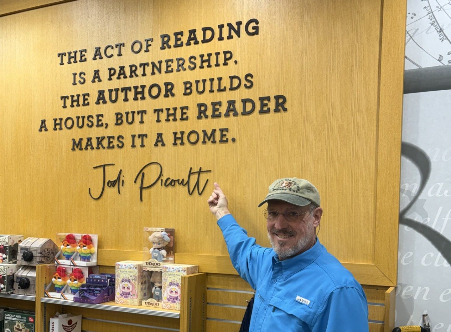 Man in blue shirt and cap pointing at wall quote in a bookstore aisle