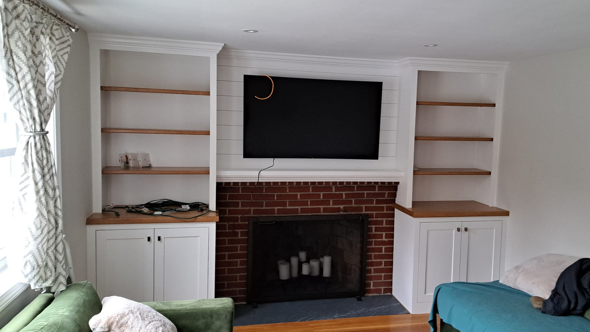 Living room with brick fireplace, built-in shelves, wall-mounted TV, and green sofa