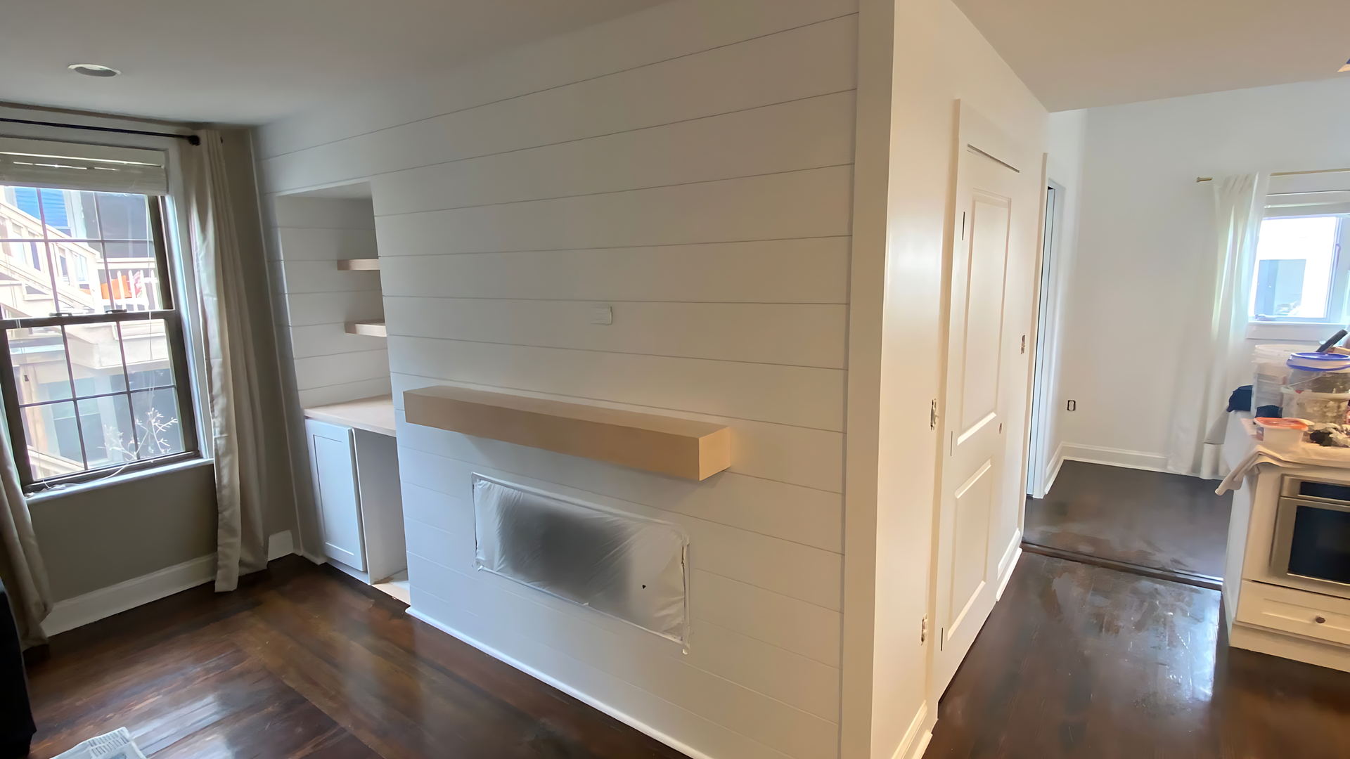 Bright empty apartment hallway with white walls, hardwood floors, and a windowed kitchen area