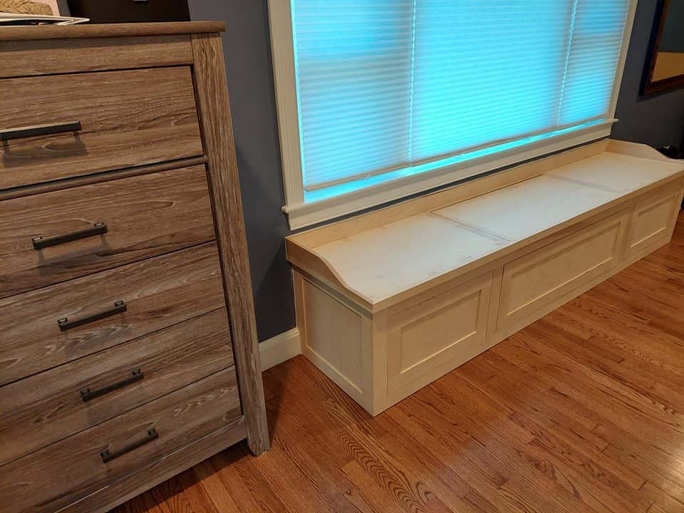 Window seat with dark cabinets, two boxes, and a plant beside a large window.