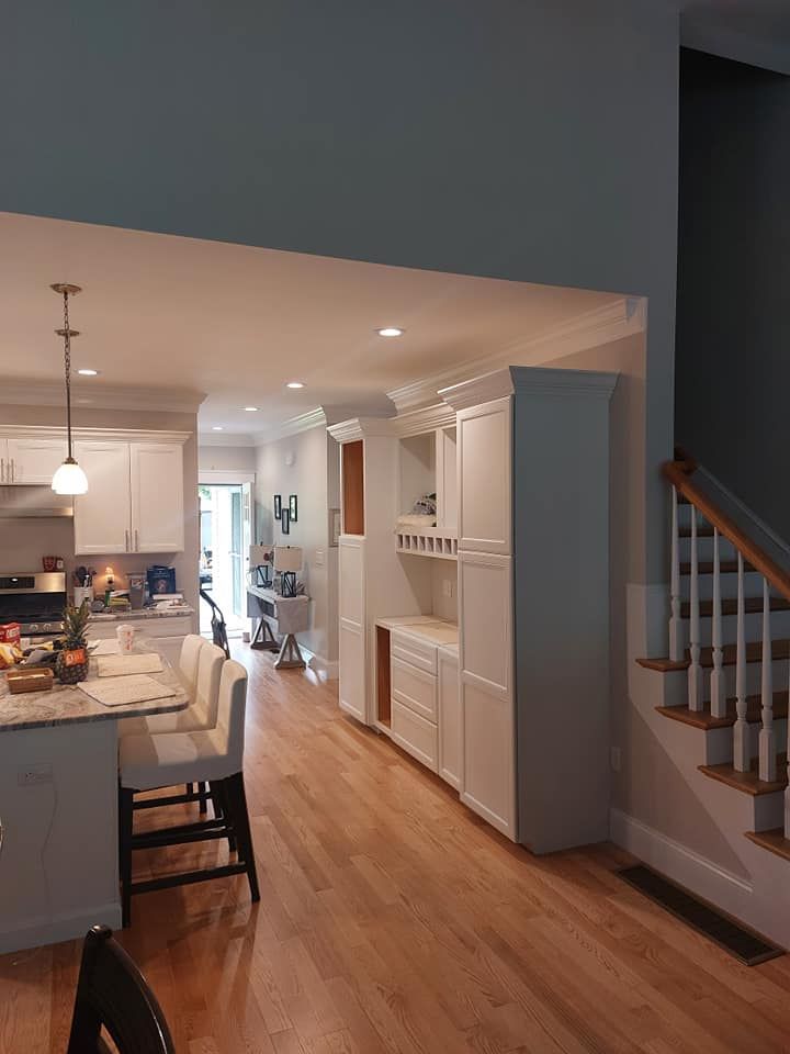 Open kitchen and dining area with hardwood floors, pendant lights, white cabinets, and staircase railing.