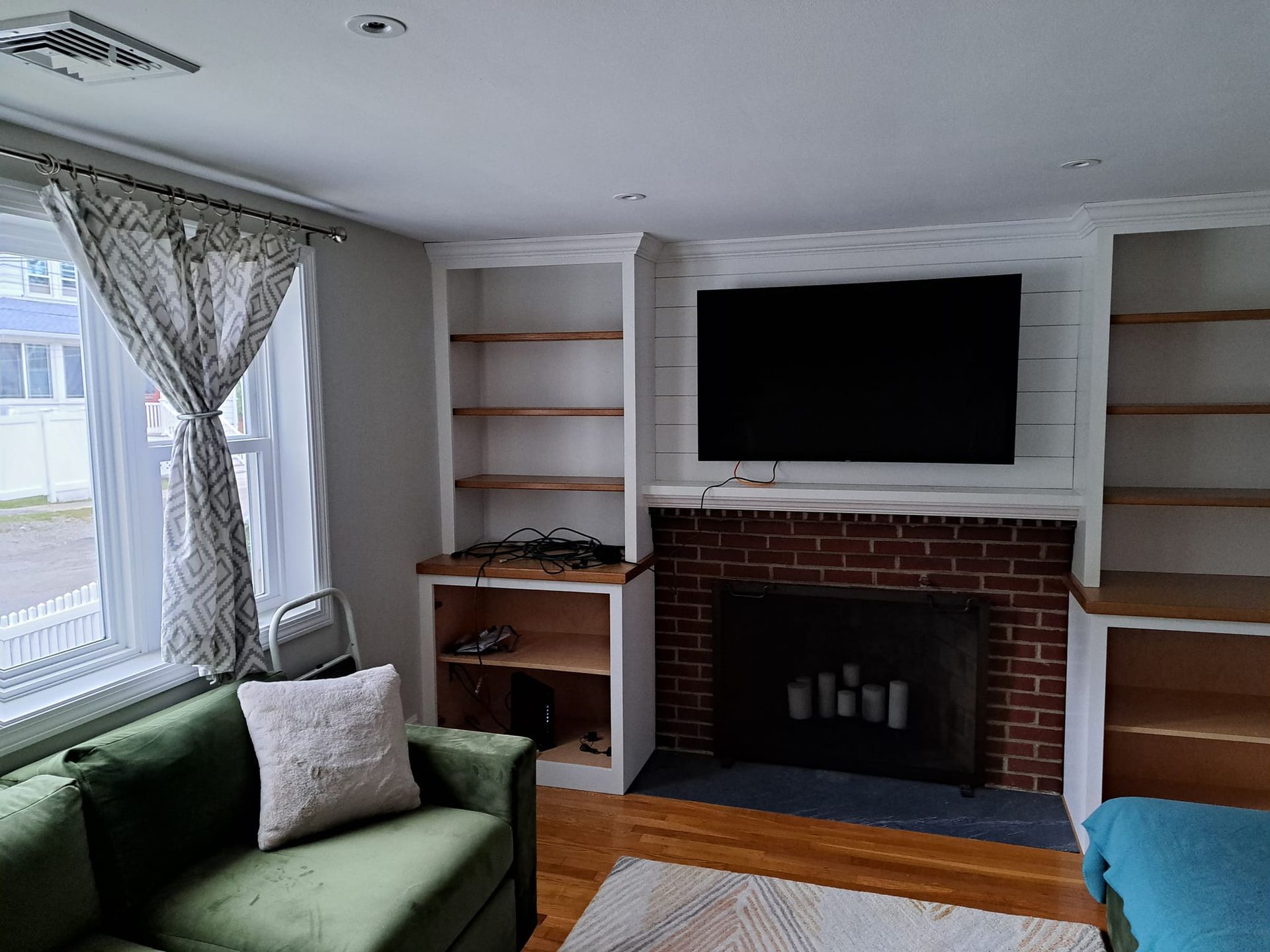 Living room with green sofa, fireplace, built-in shelves, and a TV mounted above the mantel.