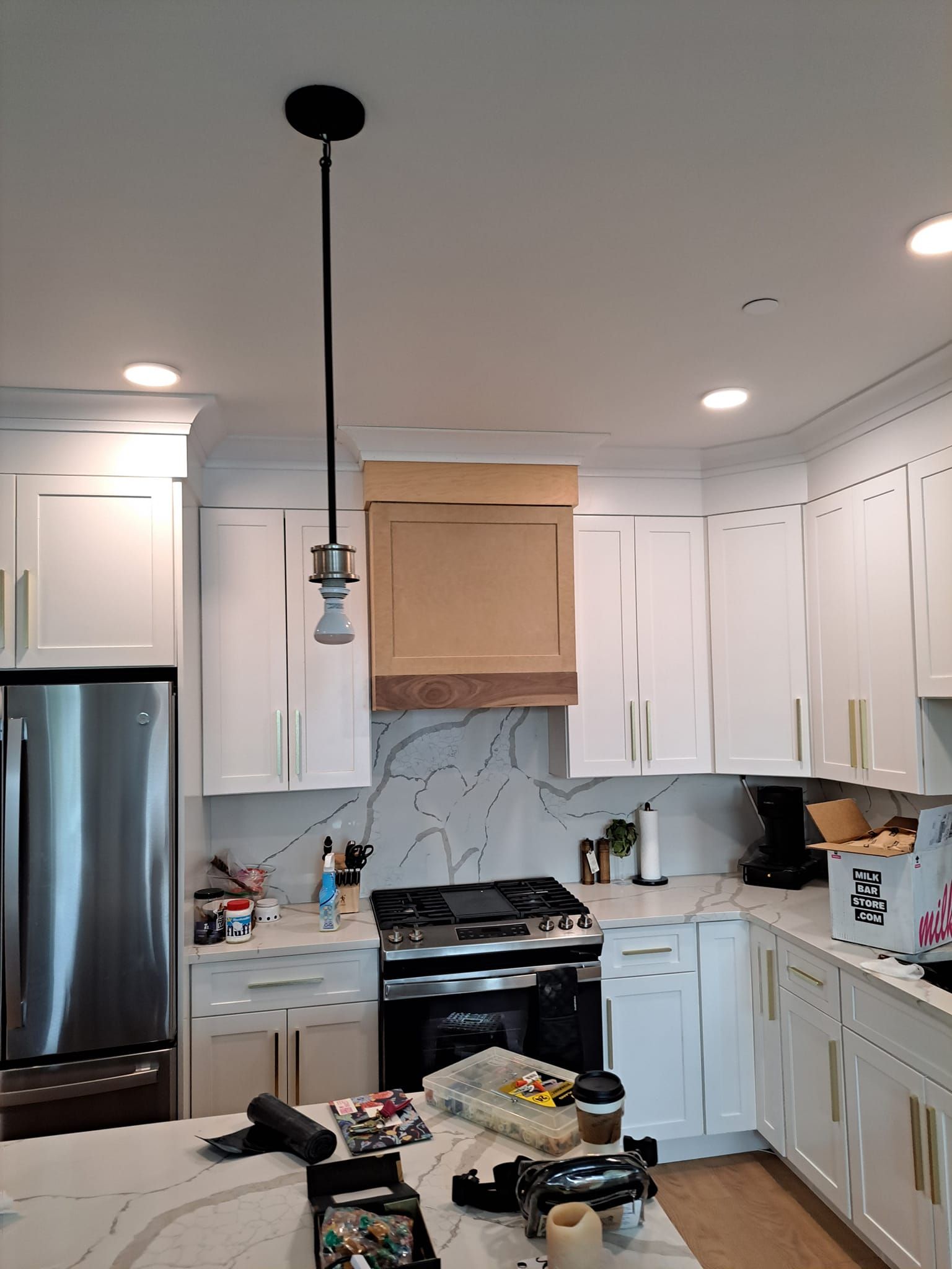 Bright white kitchen with stainless fridge, marble backsplash, island clutter, and hanging pendant light.