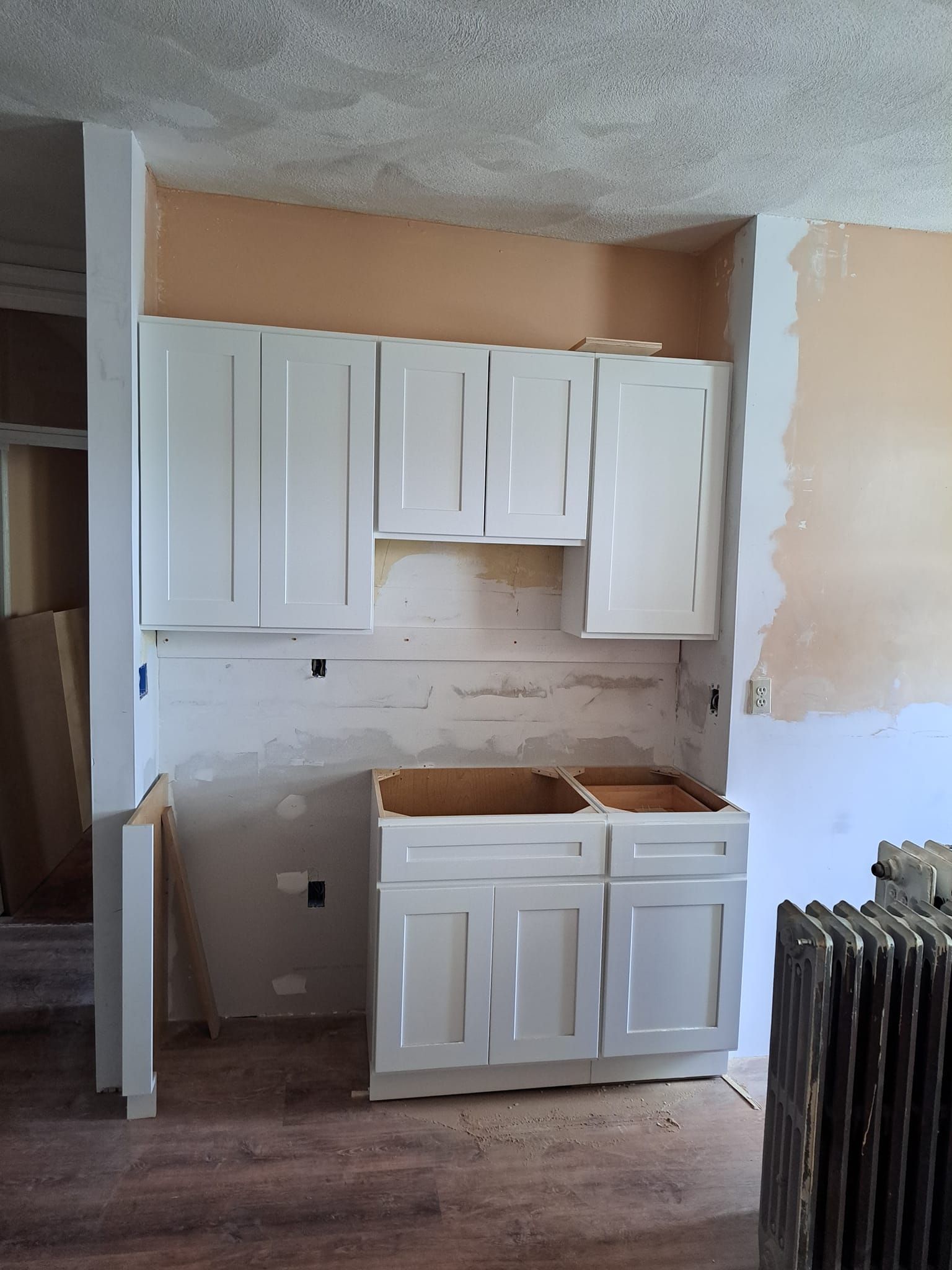Partially renovated kitchen with white cabinets, exposed wall patches, and a radiator on the right