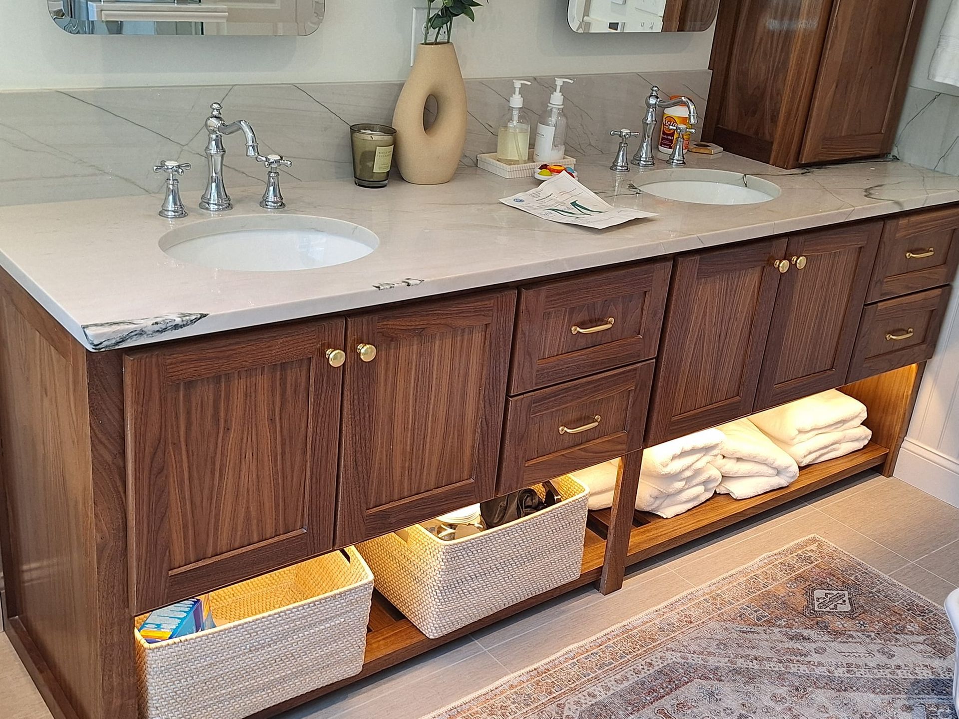 Bathroom vanity with double sink, wooden cabinets, woven storage baskets, and towels underneath.
