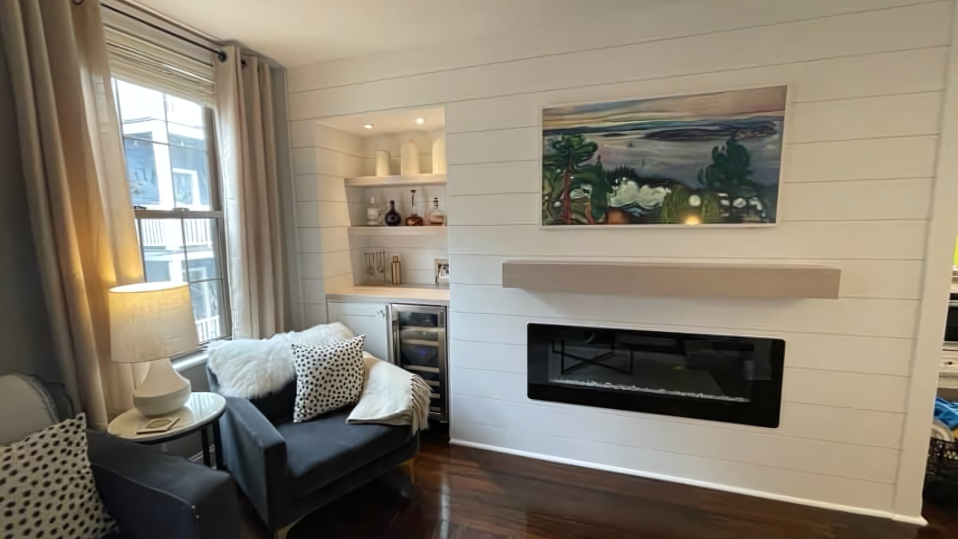 Cozy living room with armchair, fireplace, built-in shelves, window seat, and landscape painting