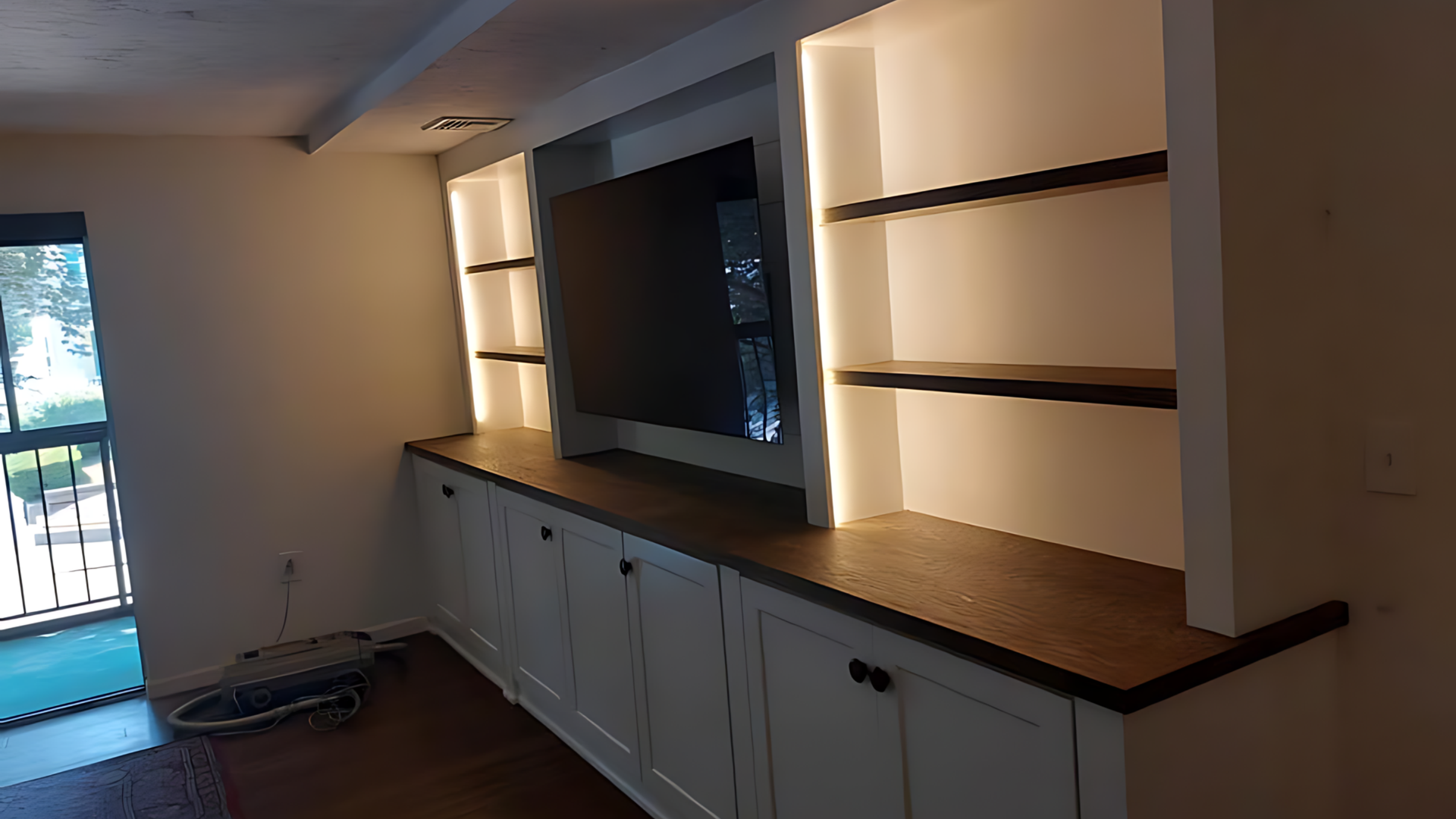 Built-in wall cabinet with wood countertop, shelves, and lower cupboards in a dimly lit room