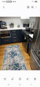 Small kitchen with dark cabinets, stainless fridge, blue runner rug, and sink by a window.