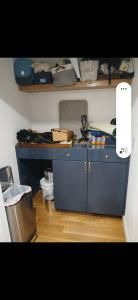 Small kitchen kitchenette with blue cabinets, countertop clutter, and shelves above.