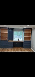 Built-in blue cabinets flanking a centered window in a room with wood floors and empty shelves