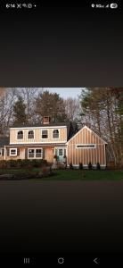 Two-story beige house with a wood-sided garage and autumn trees in the yard