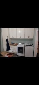 Small kitchen with white cabinets, stove, dishwasher, and countertop cluttered with items.
