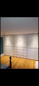 White built-in closet cabinets with drawers along a wall in a room with hardwood floor and recessed lighting