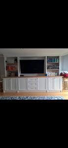 Living room media console with a large TV, white cabinets, bookshelves, and a blue rug below